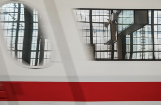 Close-up of a train’s windows as it is just beginning to leave the station. The station’s modern glass walls are reflected in the blur.