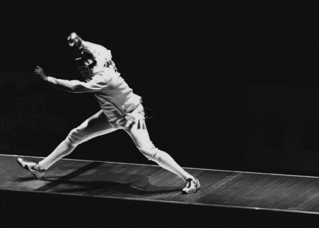 A fencer lunges forward, saber aloft.