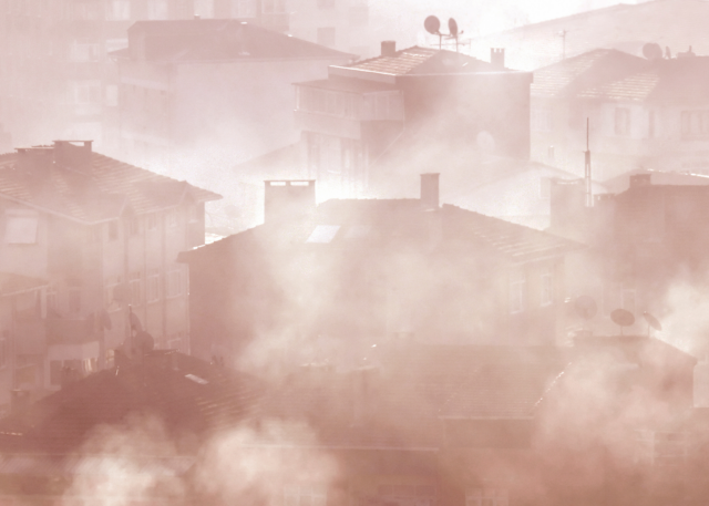 Photograph. Smoke billows out from homes in a crowded urban neighborhood.